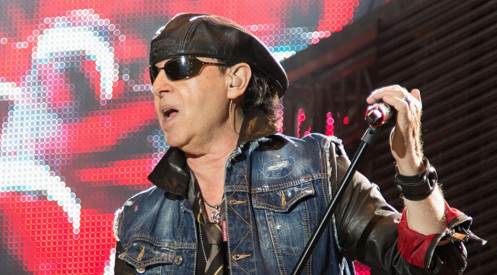 Klaus Meine performing live on stage, wearing sunglasses and a denim jacket, in a dynamic music challenge setting.