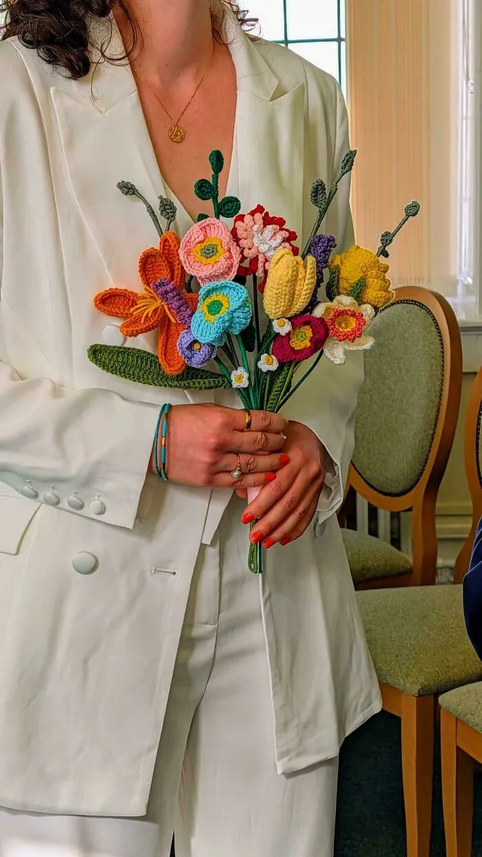 Person holding colorful crocheted flower bouquet in white suit
