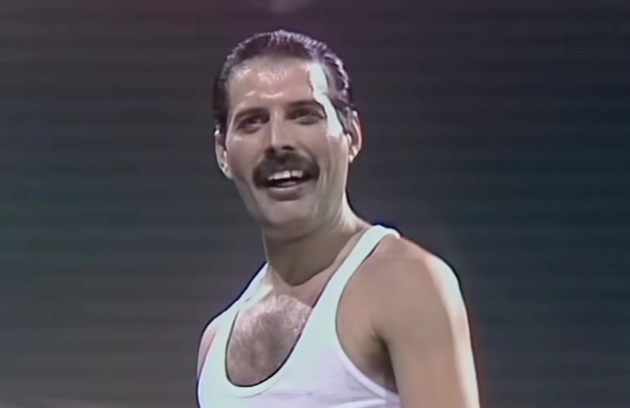 Lead singer of a 70s band performing on stage wearing a white tank top in a music challenge quiz context.