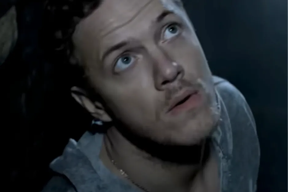 Man with blue eyes looking upward in a dimly lit setting, representing frontman and bassist of The Police.