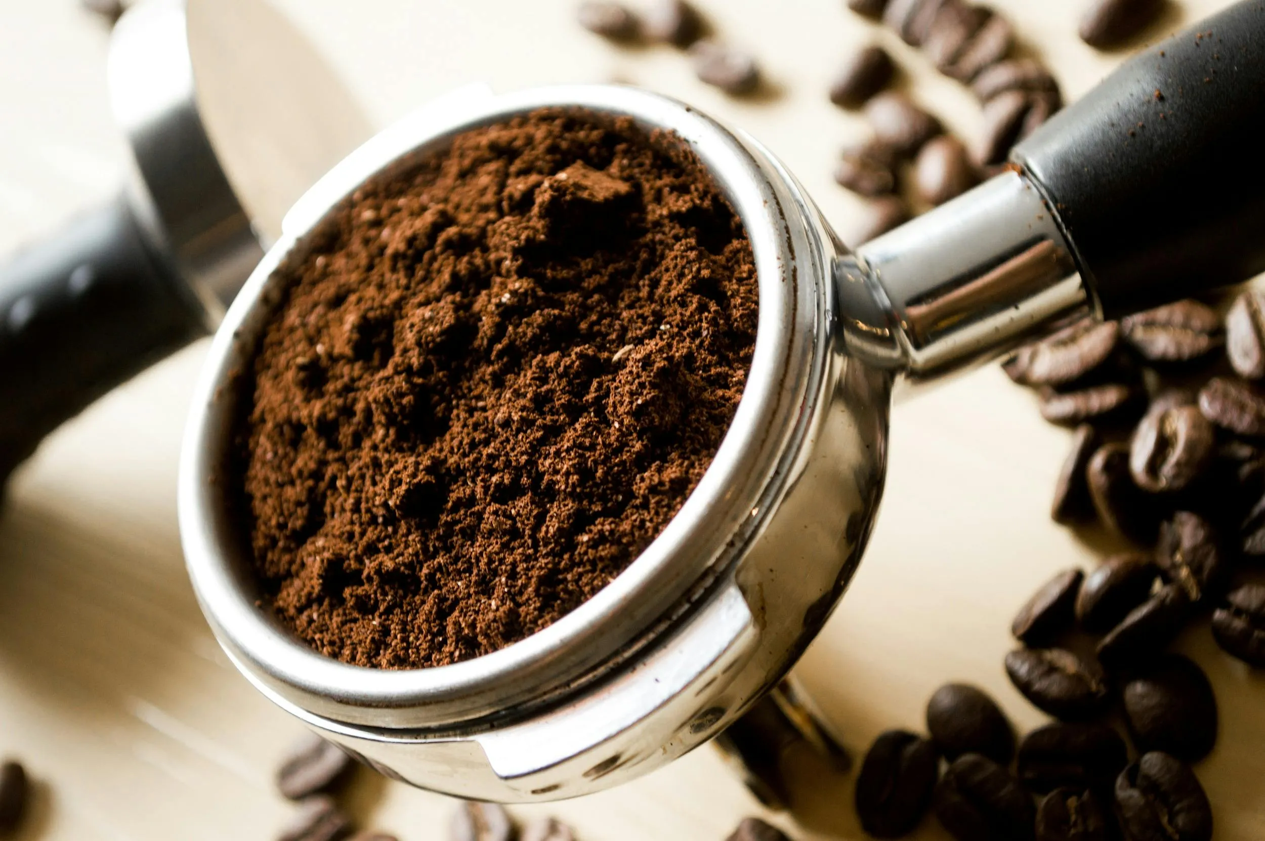 Close-up of freshly ground coffee in a portafilter surrounded by roasted coffee beans on a wooden surface
