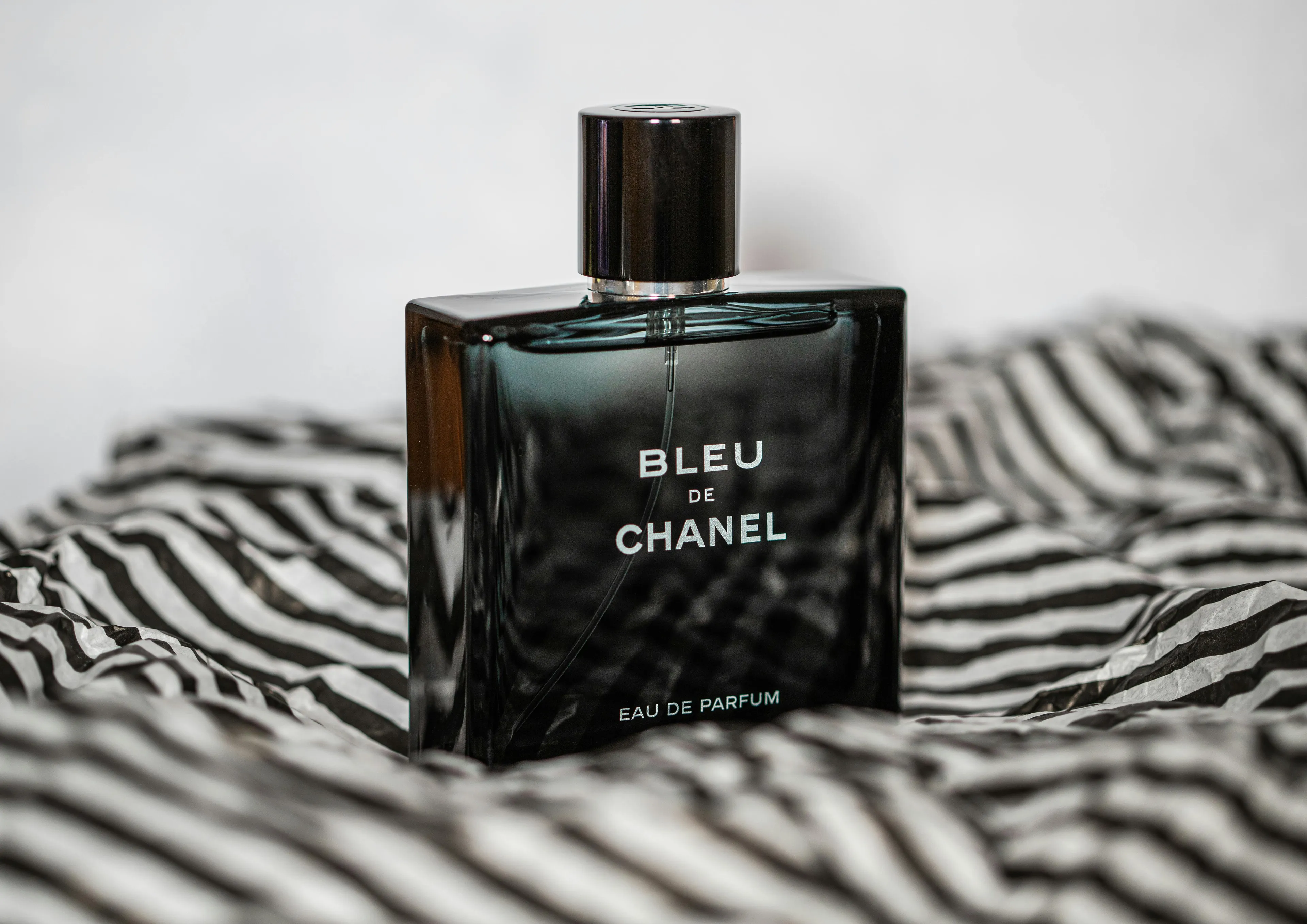 Dark glass cologne bottle labeled Bleu de Chanel placed on black and white striped fabric, evoking a stranger's scent.