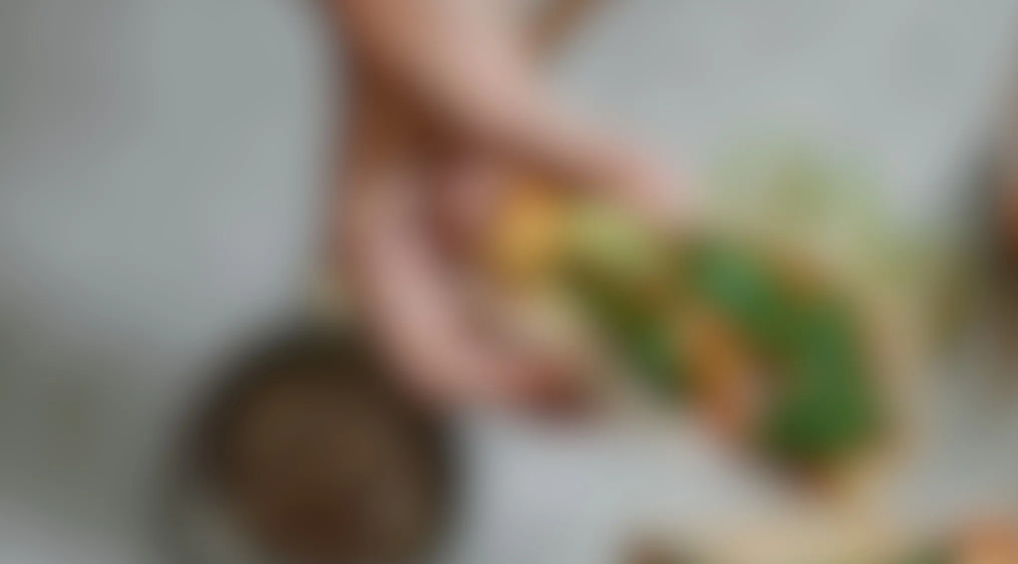Blurry image of a hand holding a Mexican dish with vibrant green and orange ingredients on a white plate