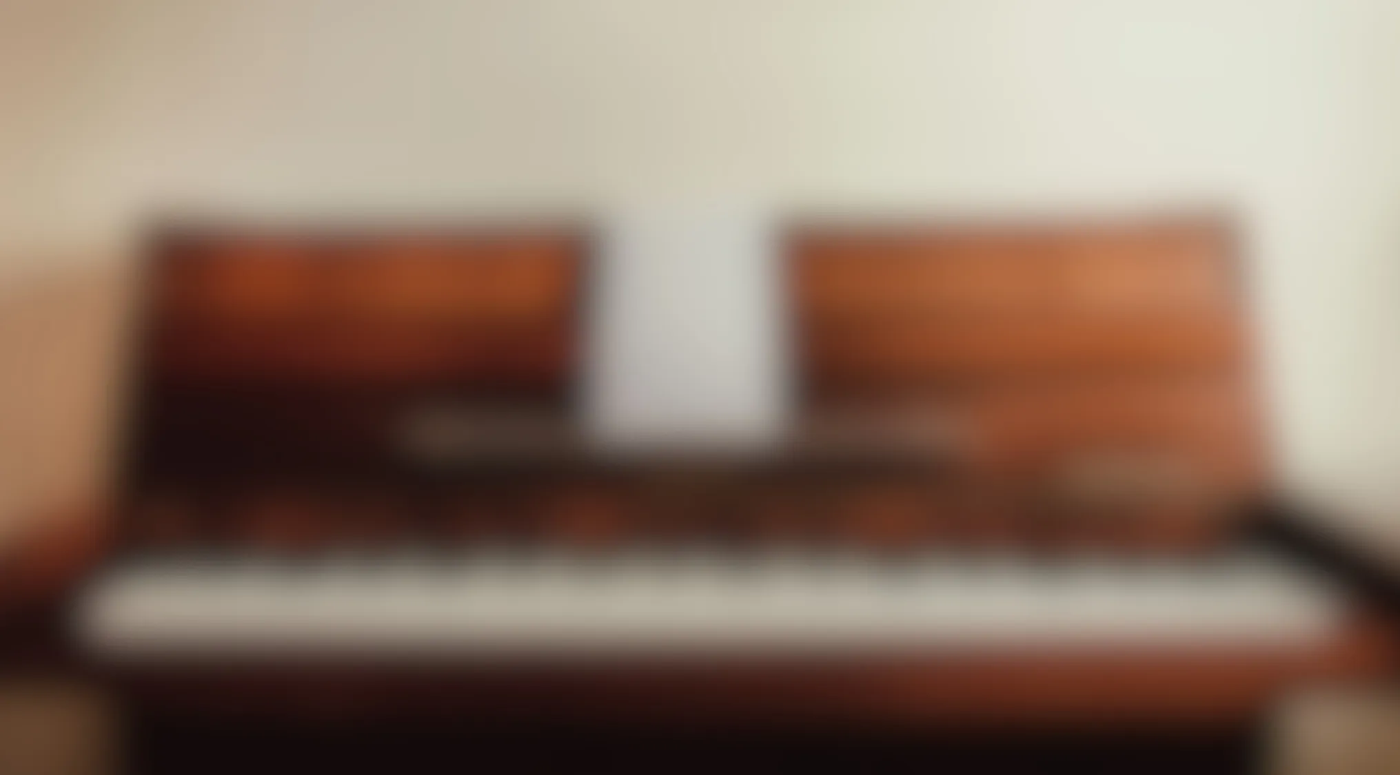 Blurry image of a wooden piano keyboard with sheet music resting on the music stand against a light background