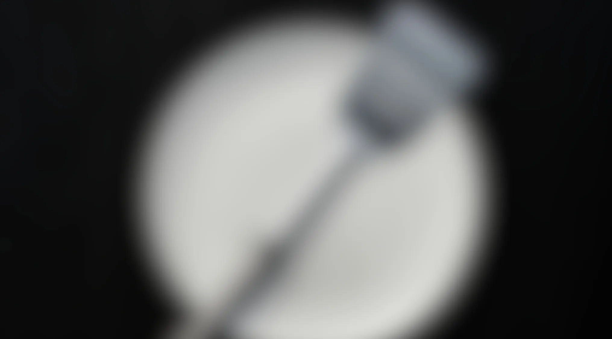 Blurry image of a kitchen utensil on a white plate with a dark background, difficult to identify the item clearly