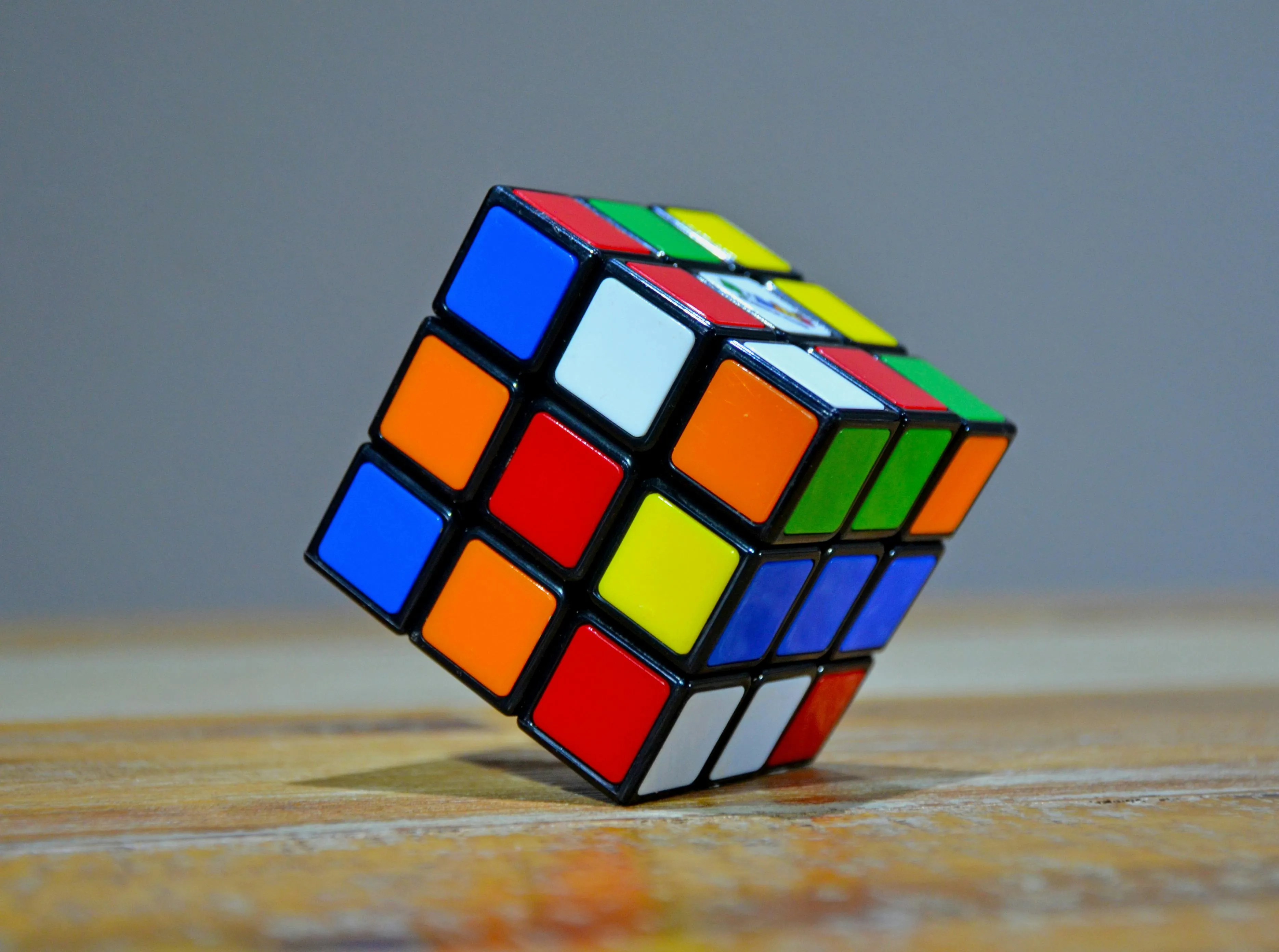 Rubik's cube resting on wooden surface with colorful scrambled squares under soft lighting.