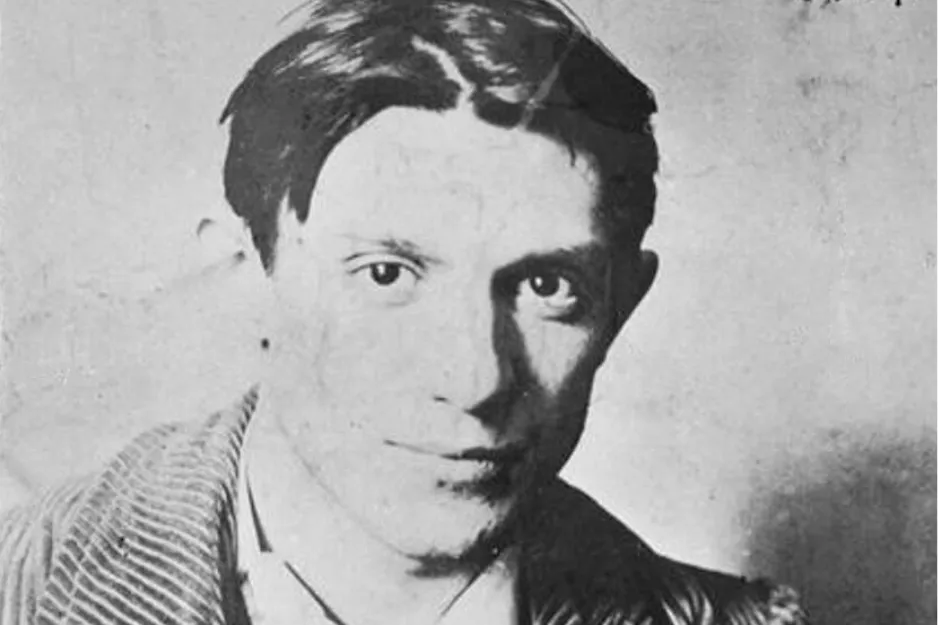 Black and white portrait of Pablo Picasso with slicked-back hair wearing a striped jacket and white shirt.