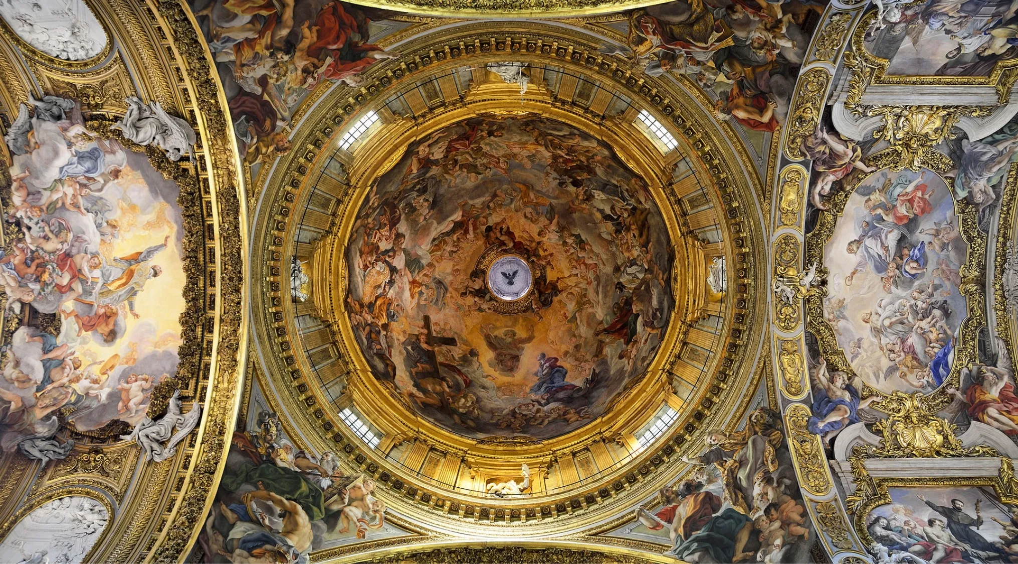 Ornate Rococo period church interior of the Church of the Gesù featuring detailed frescoes and gold embellishments on the ceiling.