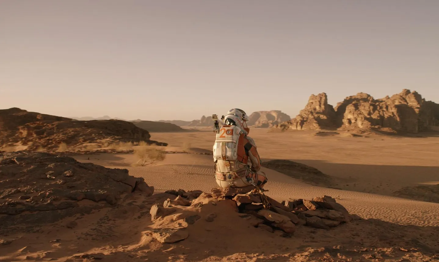 Astronaut in space suit sitting on rocky terrain in a desert landscape, related to The Martian movie cast quiz.