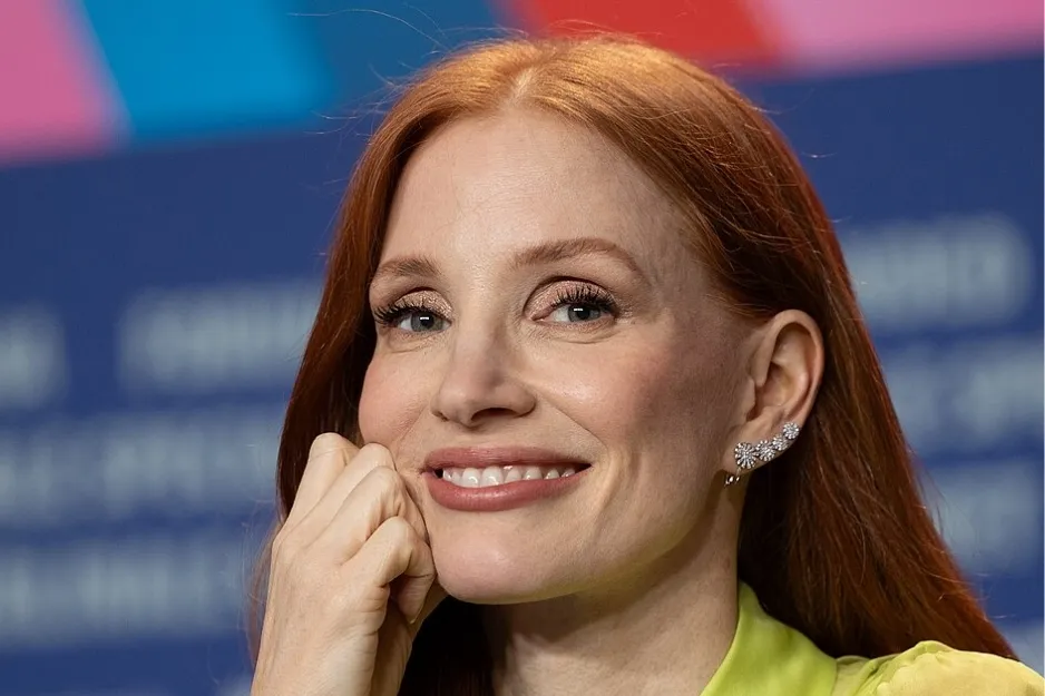 Actress Jessica Chastain smiling with red hair and wearing floral earrings at a media event for The Martian cast.