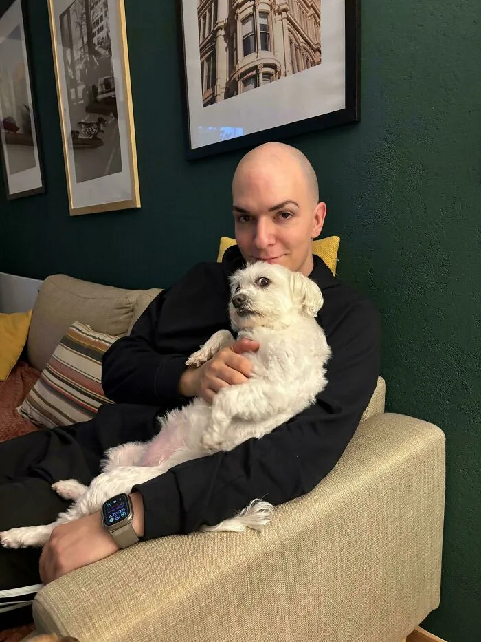 A small white dog staring intensely while sitting on a bald man's lap for funny unhinged dog pictures