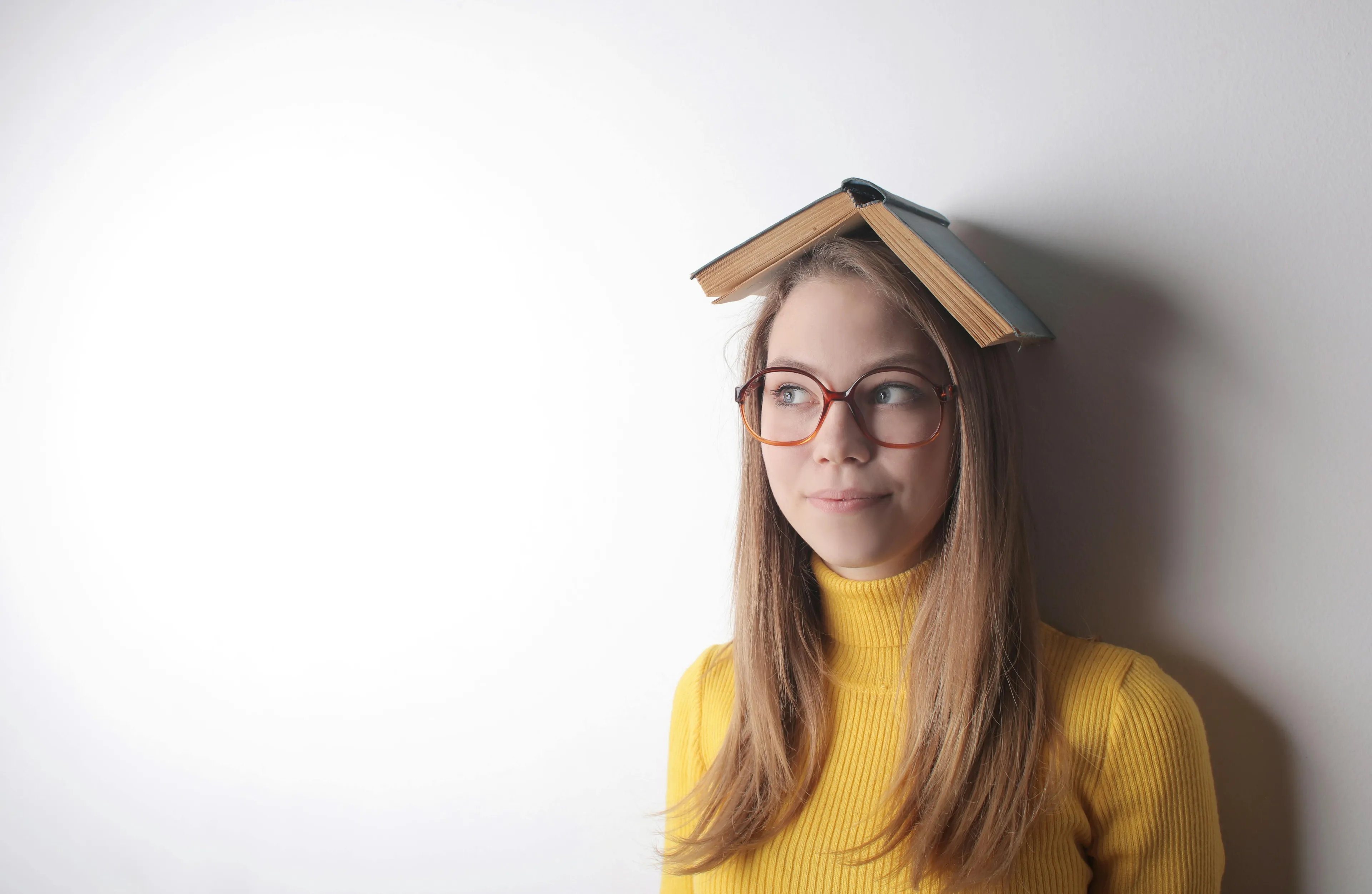 Young woman with glasses and a book on her head, symbolizing a difficult general knowledge quiz for high IQs concept.