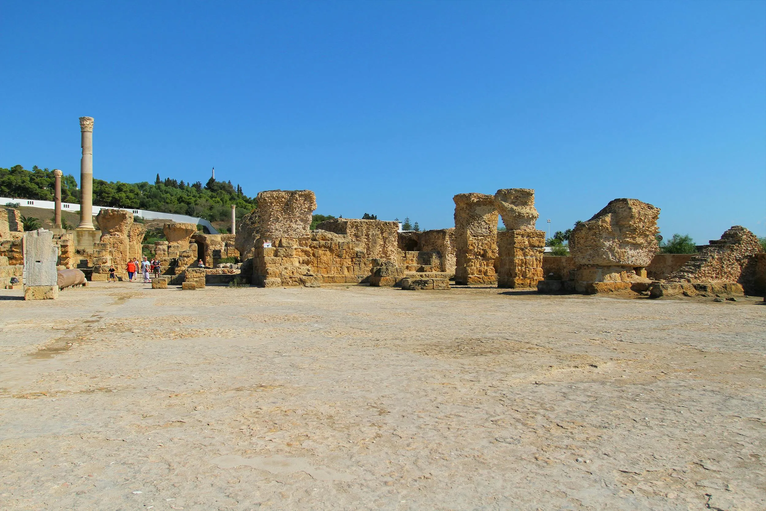 Ruins of an ancient civilization that built the city of Carthage under a clear blue sky with scattered visitors.