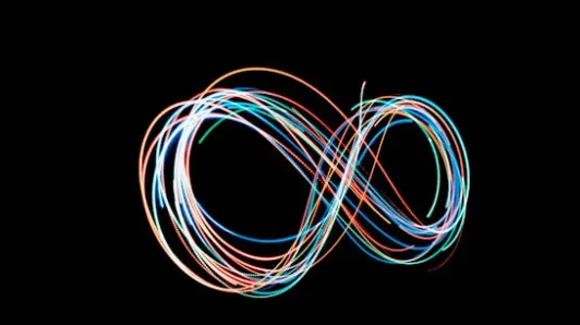 Colorful light trails forming an infinity symbol on a black background representing a shape with infinitely many sides in math.