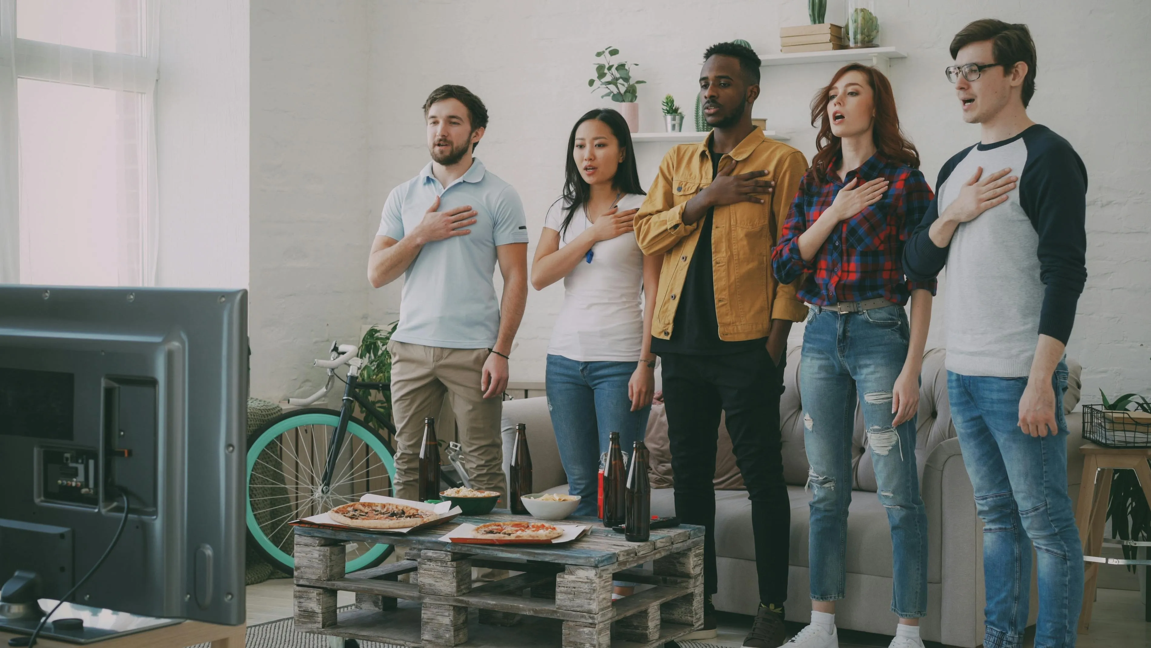 Group of young adults standing with hands over hearts watching a screen about which country has a national anthem without words quiz.