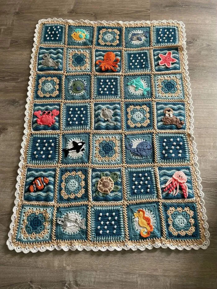 Crocheted ocean-themed blanket with animal and floral motifs on wooden floor