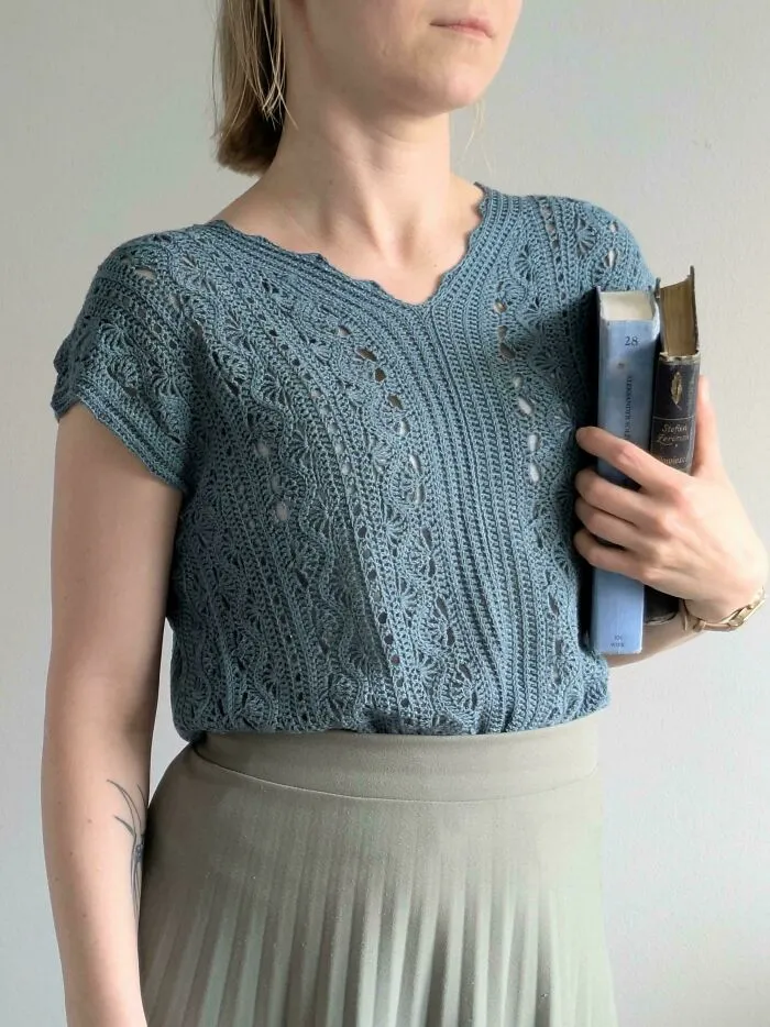 Woman wearing a blue crocheted top holding books showcasing crocheters' talent