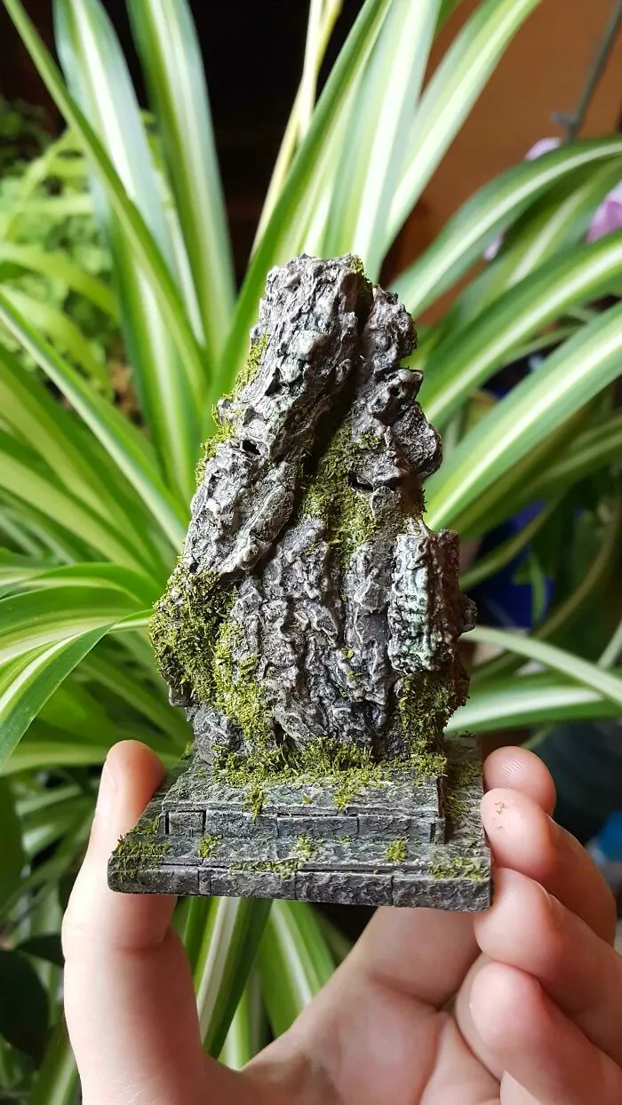 Hand holding a small, moss-covered trash rock sculpture, embodying creative people transforming trash into something artistic.