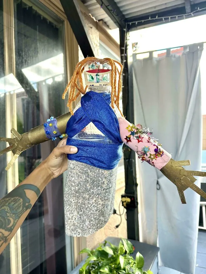 A creative person holds a doll made from trash, illustrating artistic reuse of everyday items.