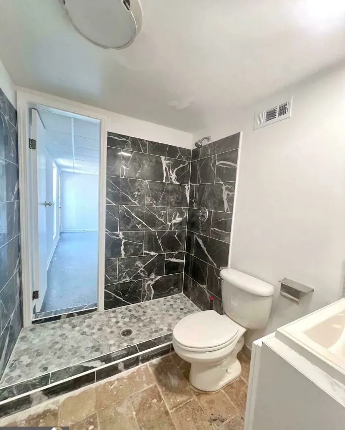 Baño mal reformado con una puerta de ducha extraña.