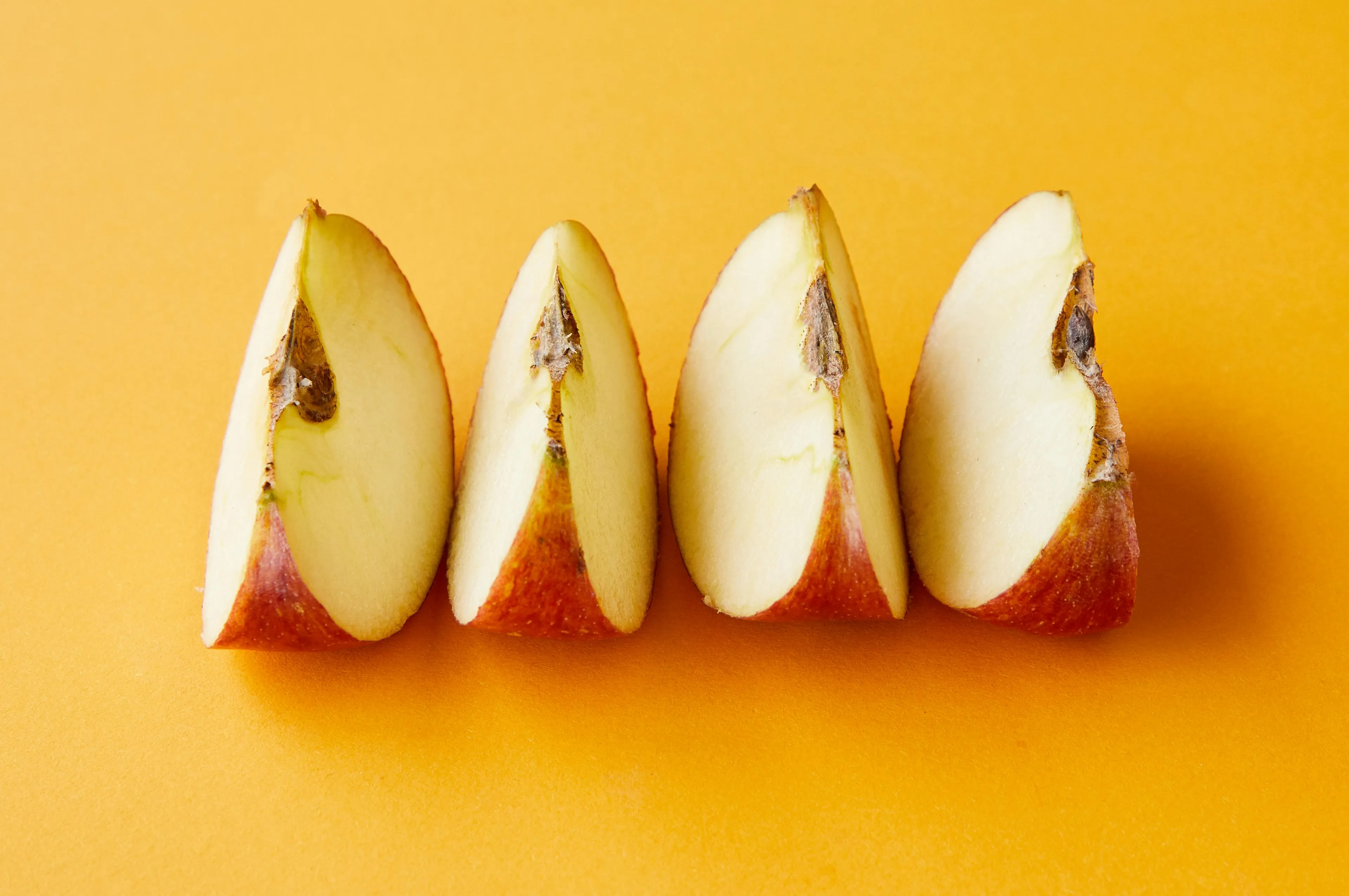 Four fresh apple slices arranged on a vibrant orange surface, perfect snack for emergencies and on-the-go.