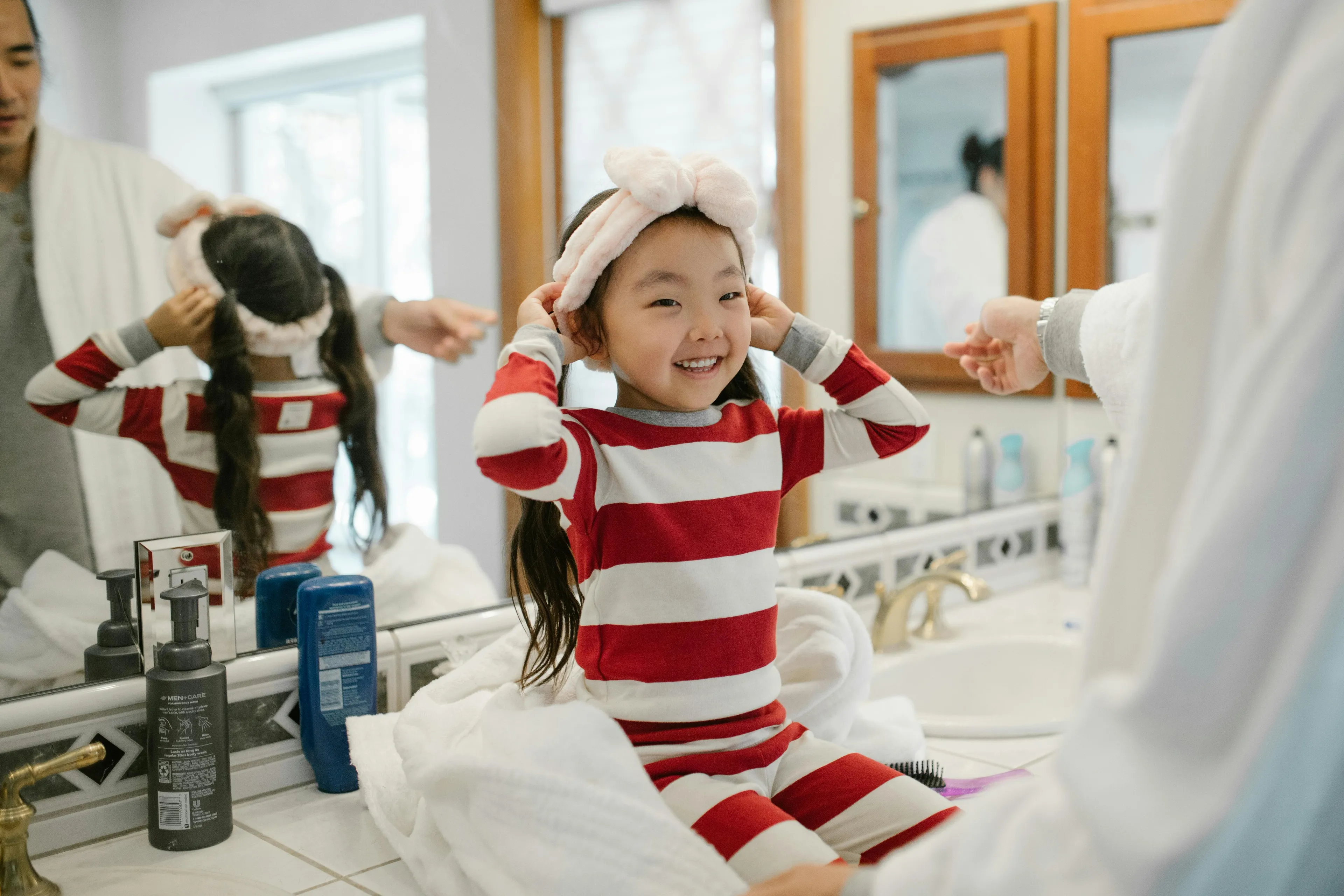 Child in striped pajamas smiling during early morning routine with the kids at the bathroom sink.