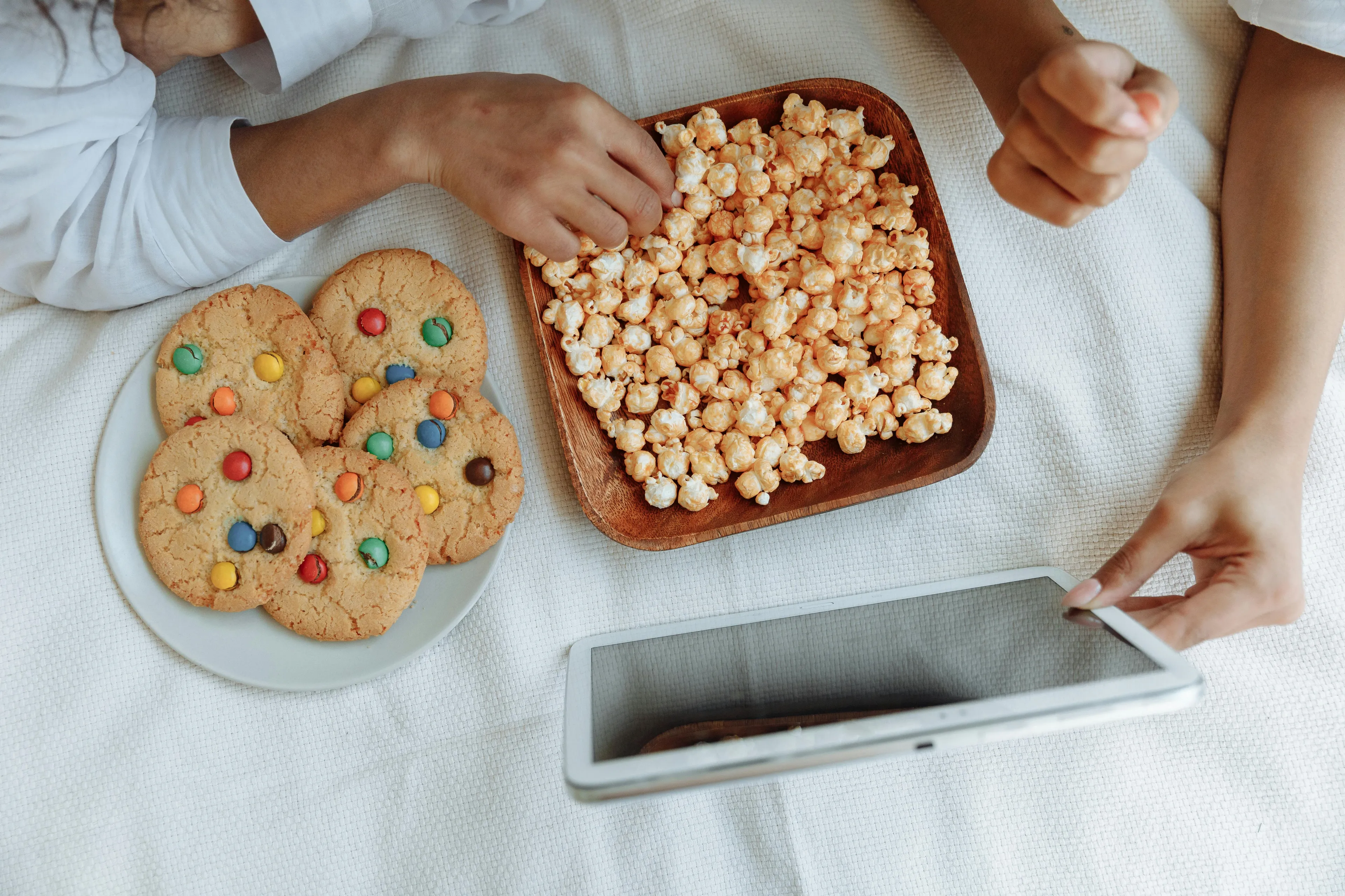 Children enjoying late-night snacks of popcorn and cookies while using a tablet in a cozy setting.
