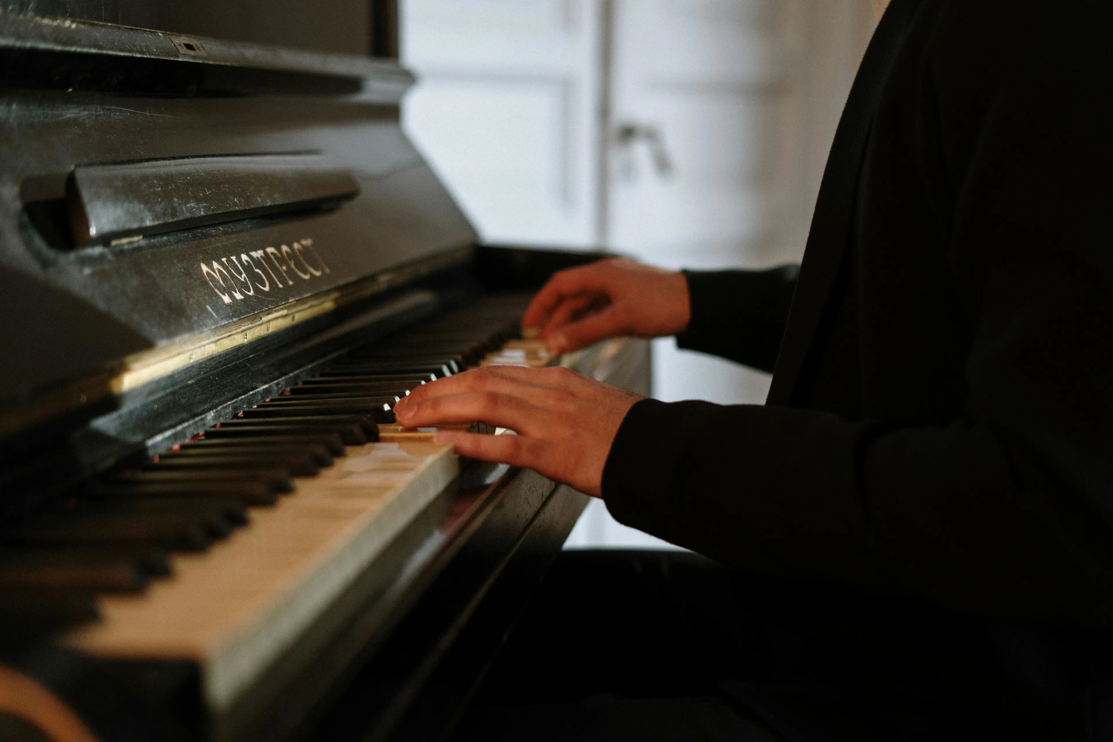 Person playing an old Mystic piano, hands pressing keys with focus on the musical instrument and its vintage design.