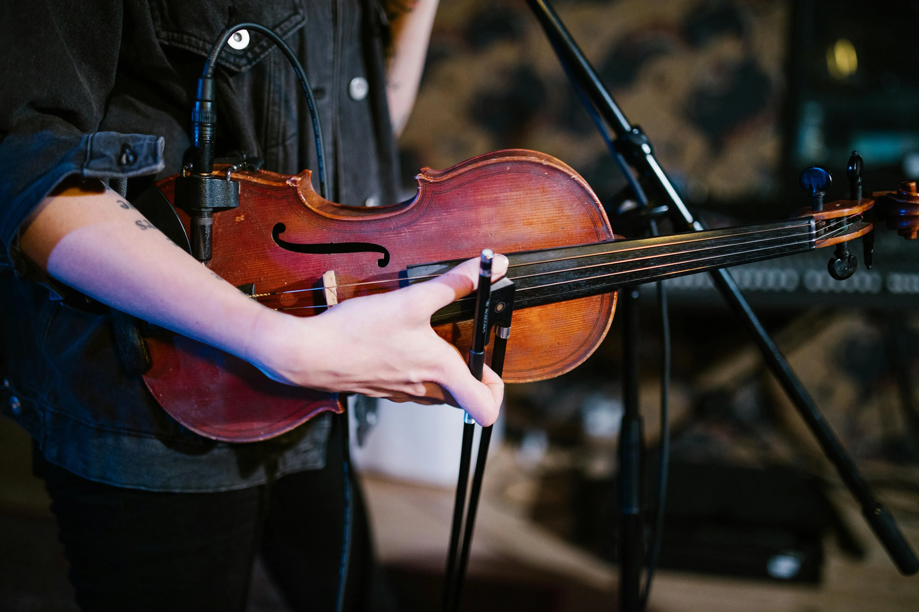 Person holding and playing a violin with a microphone attached, focusing on the instrument and hand positioning.