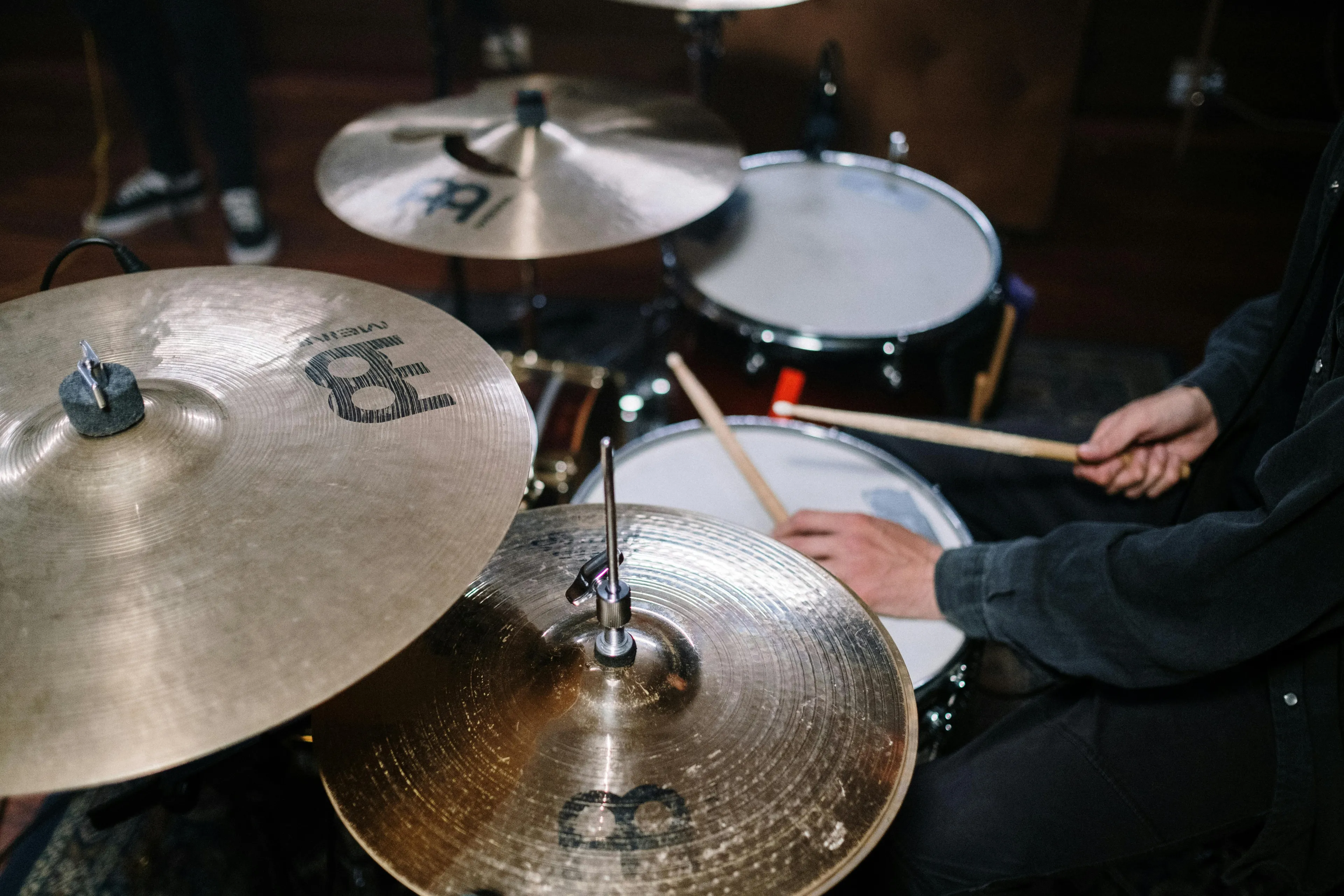 Close-up of a person playing drums with drumsticks, focusing on cymbals and snare drum in a music studio.
