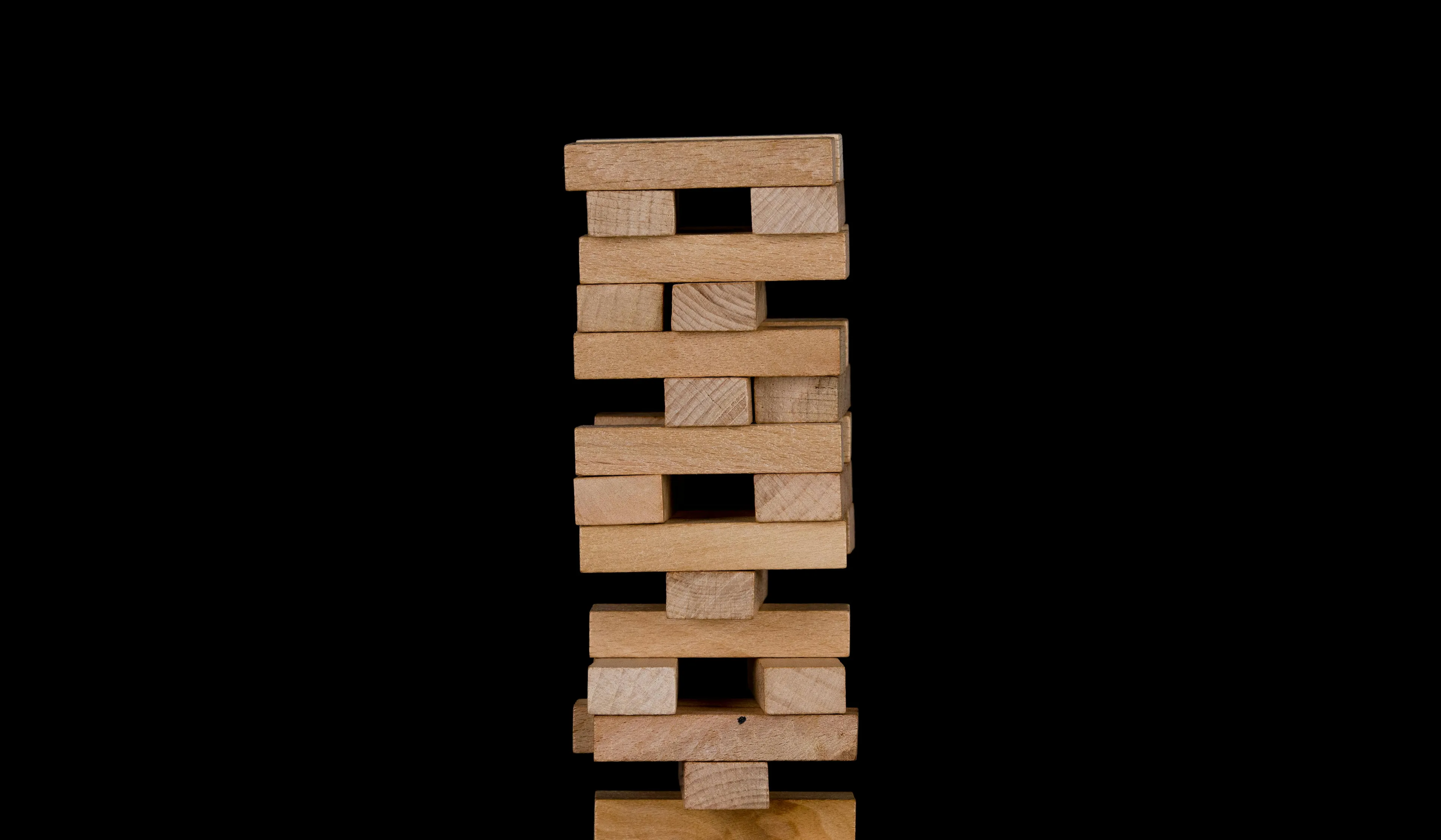 Tower of wooden blocks stacked unevenly for a classic board game Jenga on a plain black background.