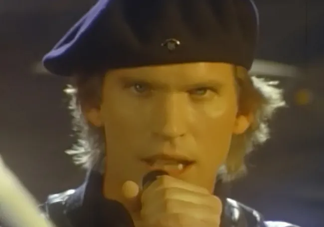 Close-up of a singer wearing a beret performing Eye of the Tiger, a powerful anthem for your parenting playlist.