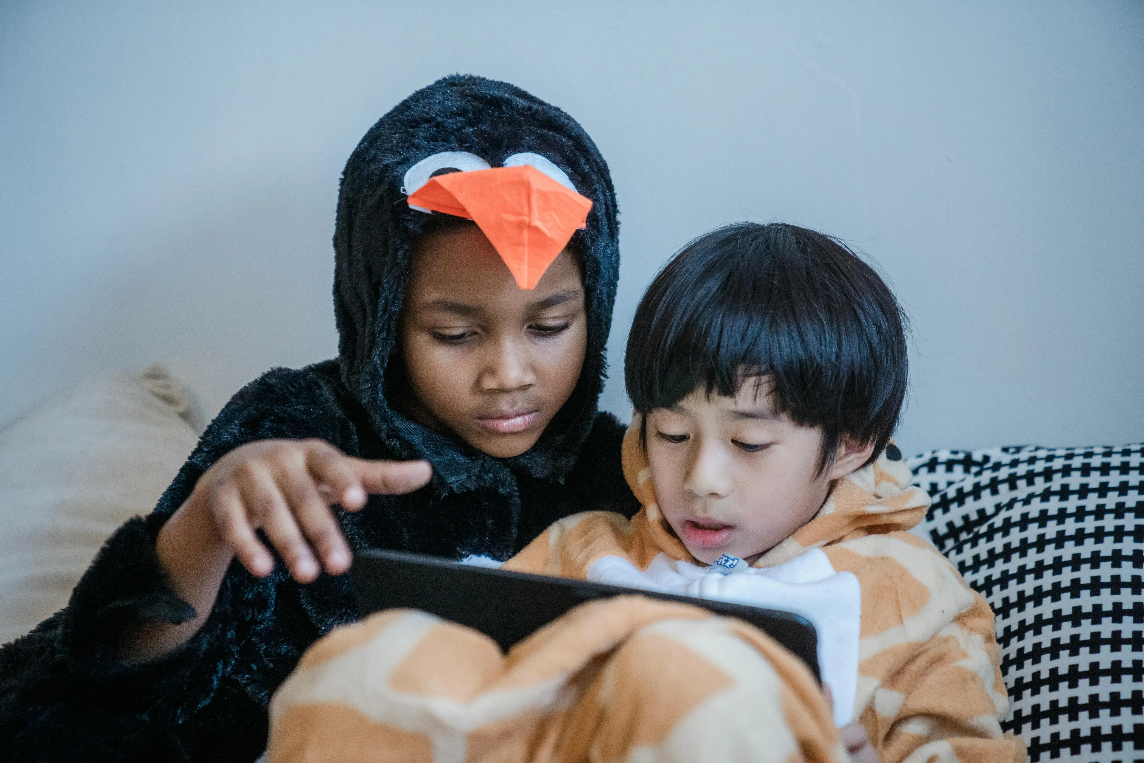 Two children in cartoons in pajamas using a tablet together, enjoying a cozy weekend family activity at home.