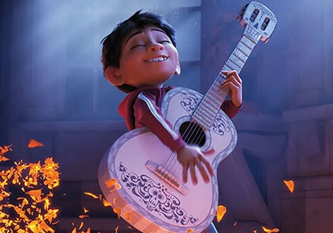 Animated character from Coco joyfully playing a white guitar surrounded by glowing orange petals in a dimly lit room.