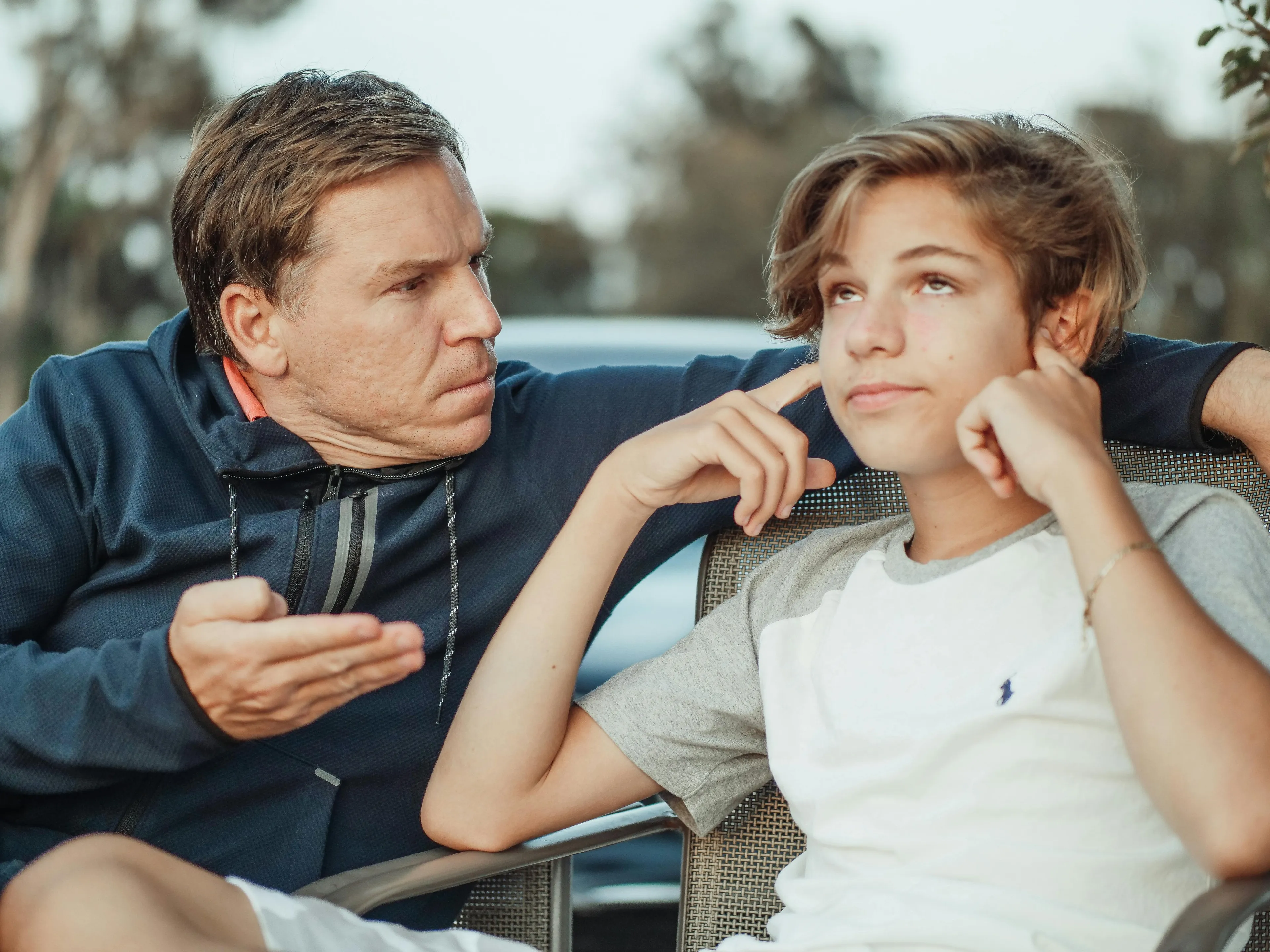 Father and teen having a serious conversation outdoors about parenting style and negotiating a later curfew request.