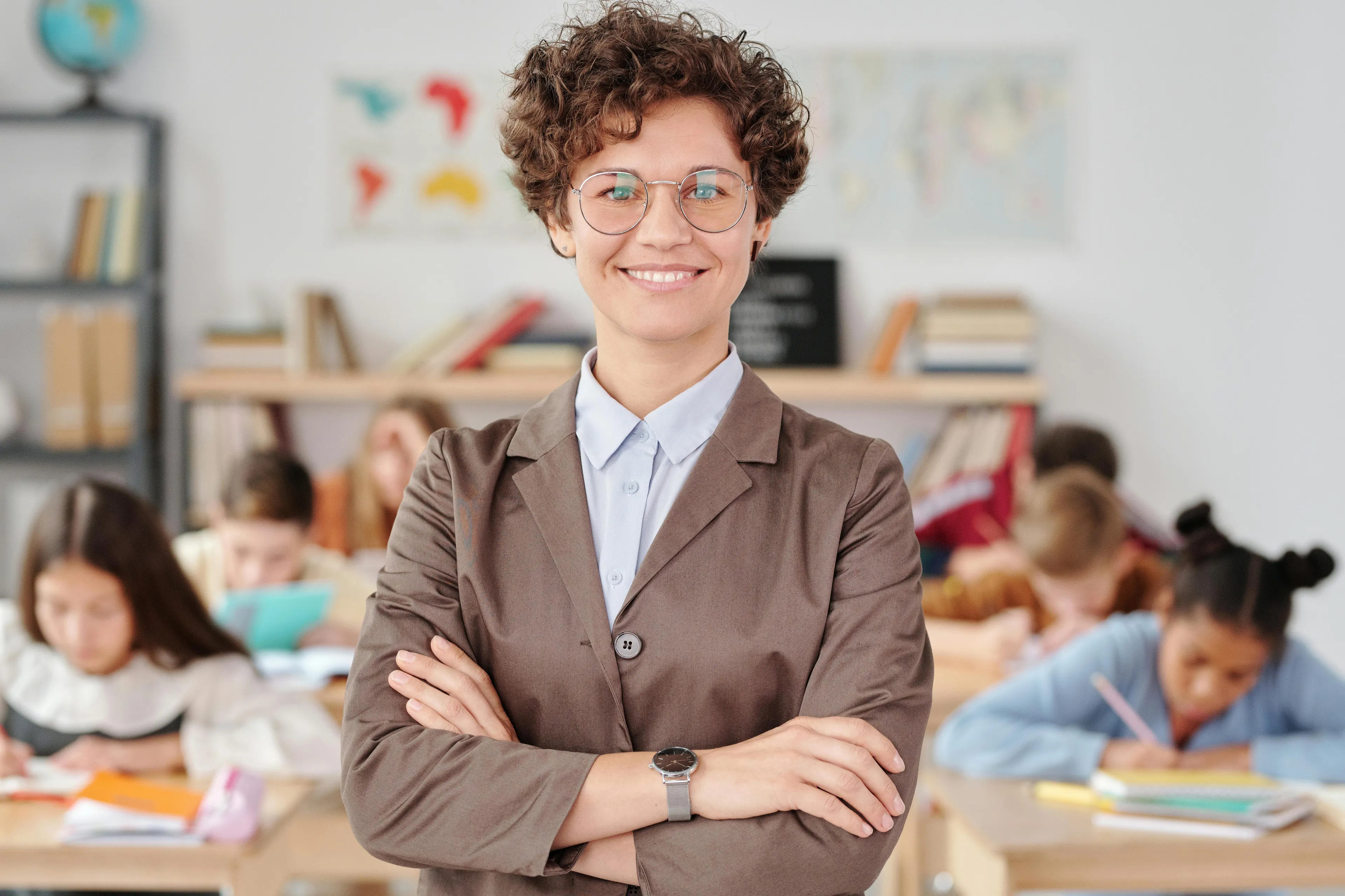 Teacher with glasses standing confidently in classroom during parent-teacher conference about parenting styles.
