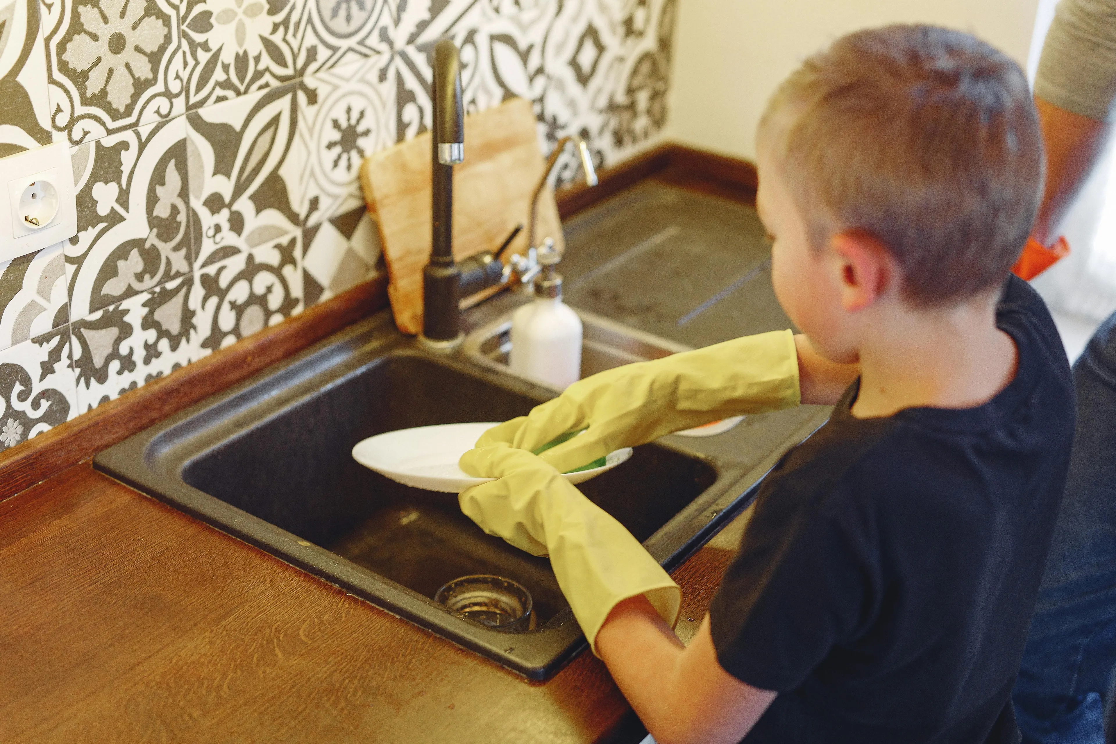 Child washing dishes in kitchen demonstrating household chore delegation style related to parenting style.