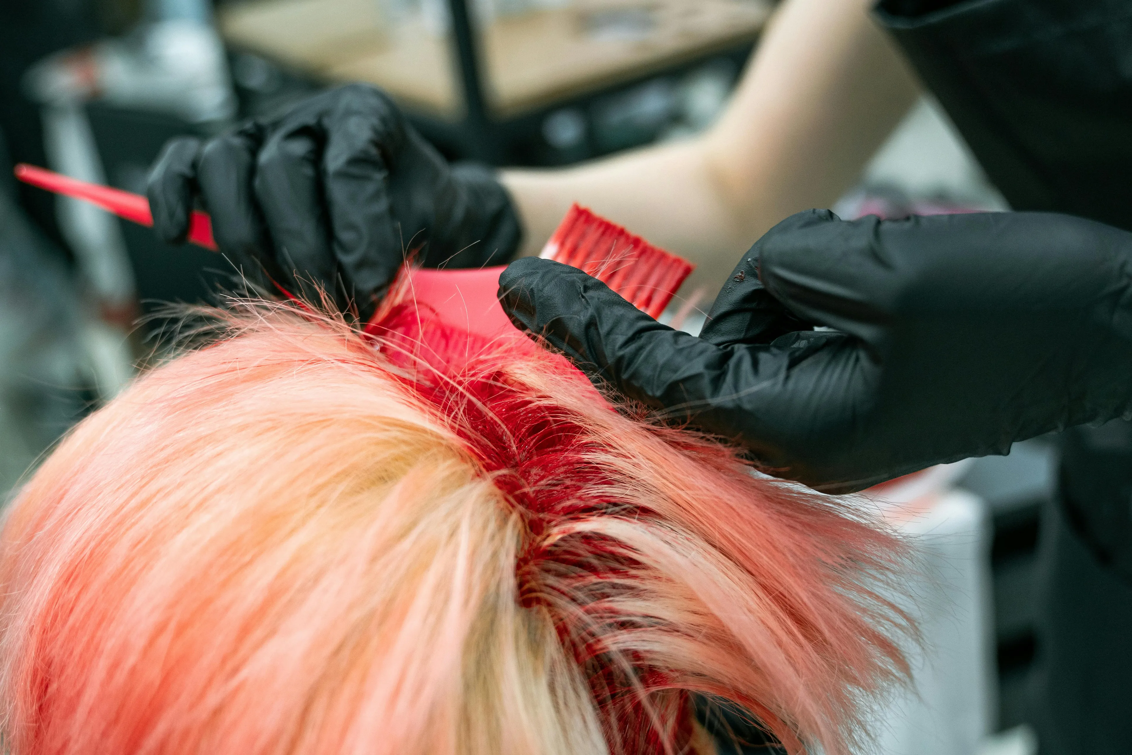 Teen having neon red hair dye applied by a hairstylist wearing black gloves, reflecting parenting style reactions.