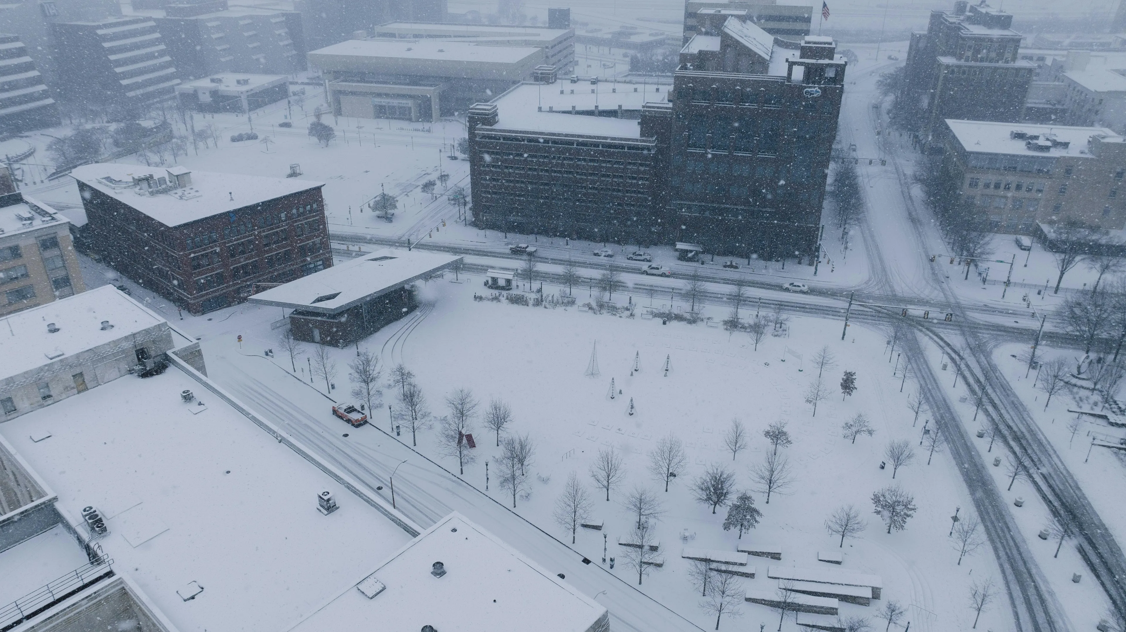 A snowy urban park and streets covered in fresh snow during a snow day announcement in a city setting.