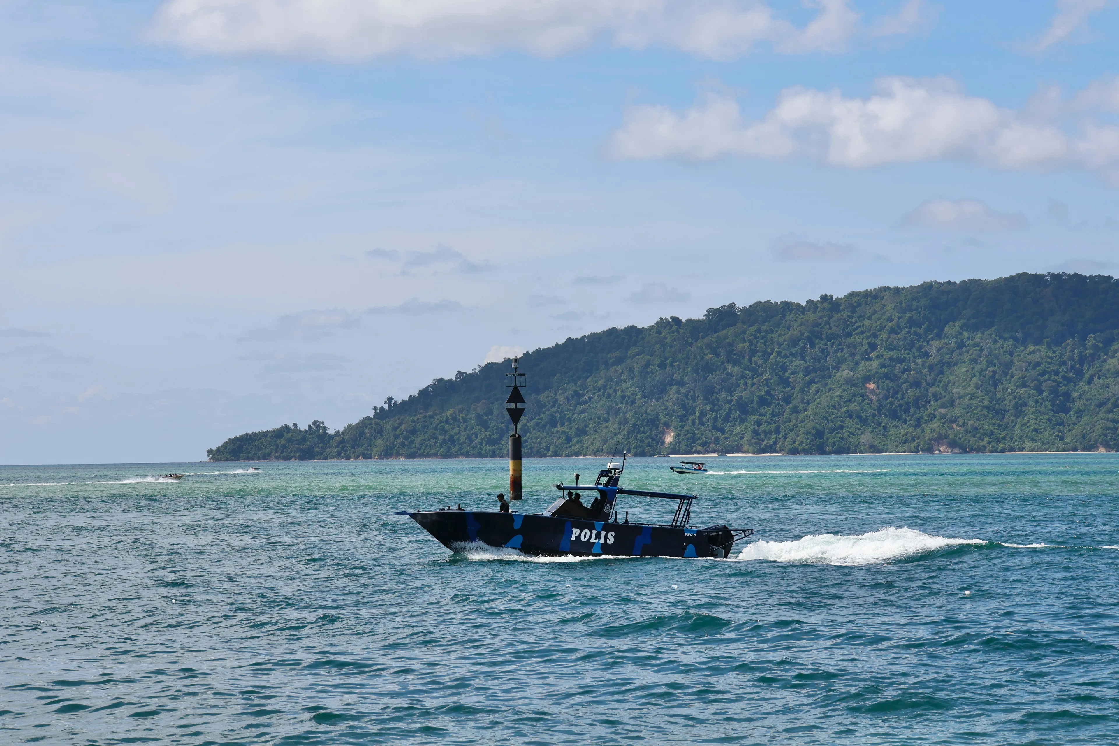 Coast guard boat patrolling near a coastline with lush hills, highlighting geography and countries sharing a land border.