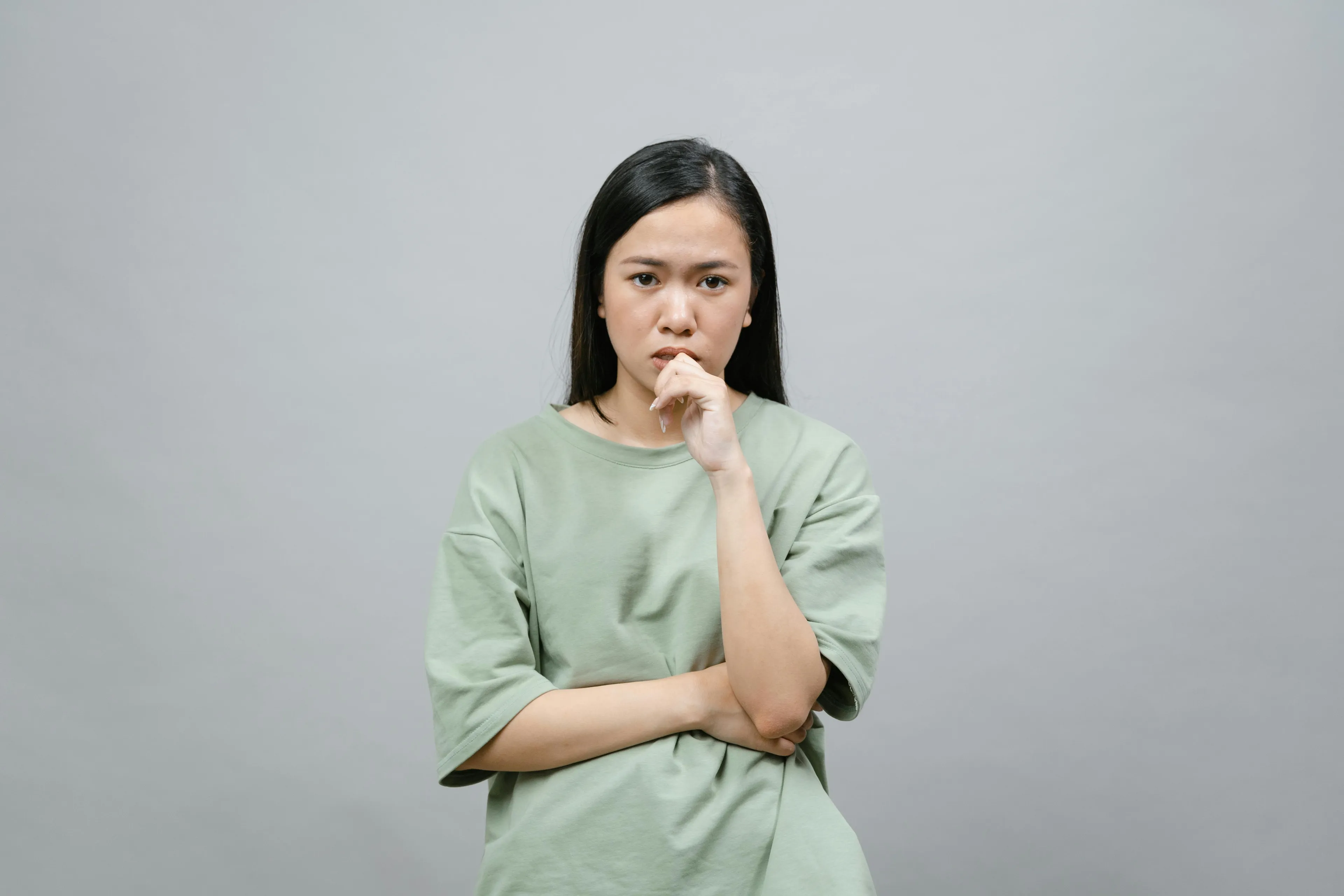 Young woman in a green shirt thinking deeply about which countries the Baltic states include for geography quiz.