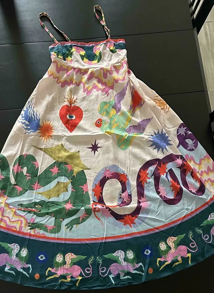 Vibrant white dress with whimsical dragon, heart, and mythical creature illustrations, a fabulous thrift store jackpot.