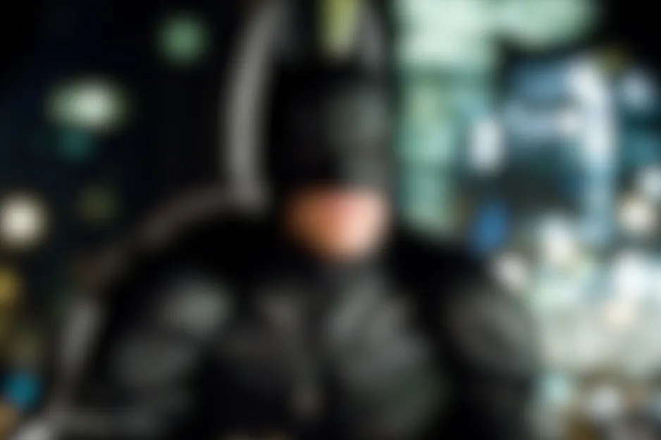 Blurred image of Batman showing his cowl and cape against a dark, lit background.