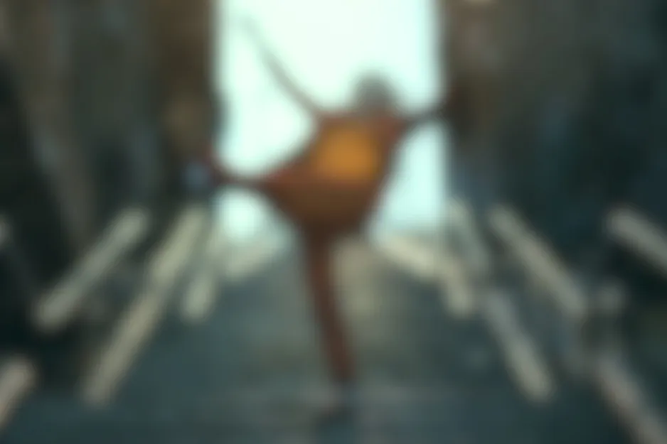 Blurred scene from Joker (2019) featuring a figure in a reddish suit, mid-pose with arms out and one leg raised.