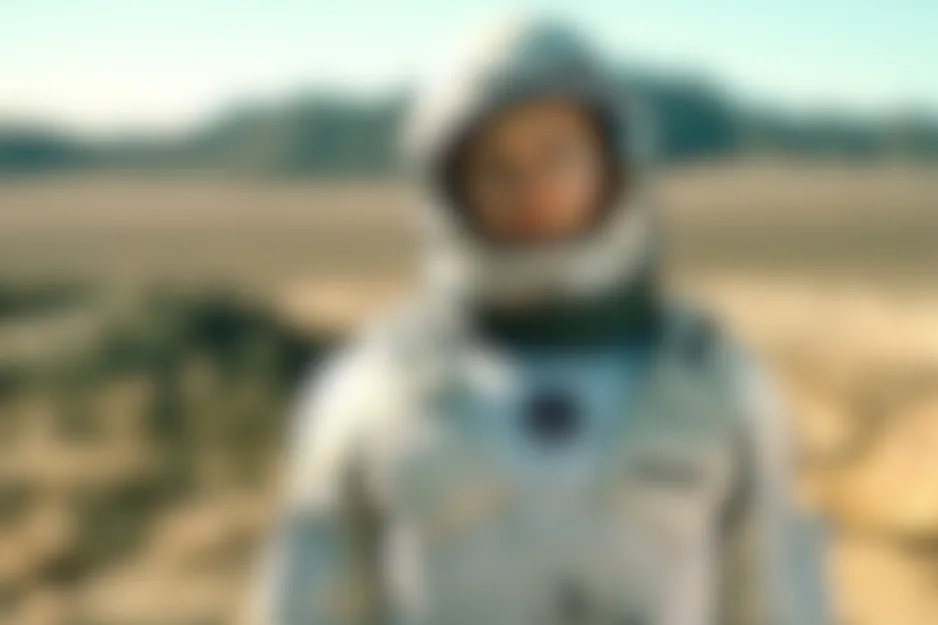 Blurred Interstellar scene showing a character in a white hooded suit against a vast, desolate, snow-covered landscape.