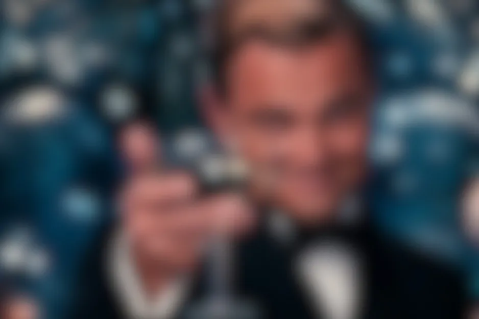 Blurred scene from Catch Me If You Can (2002) featuring Leonardo DiCaprio in a tuxedo, smiling and pointing.