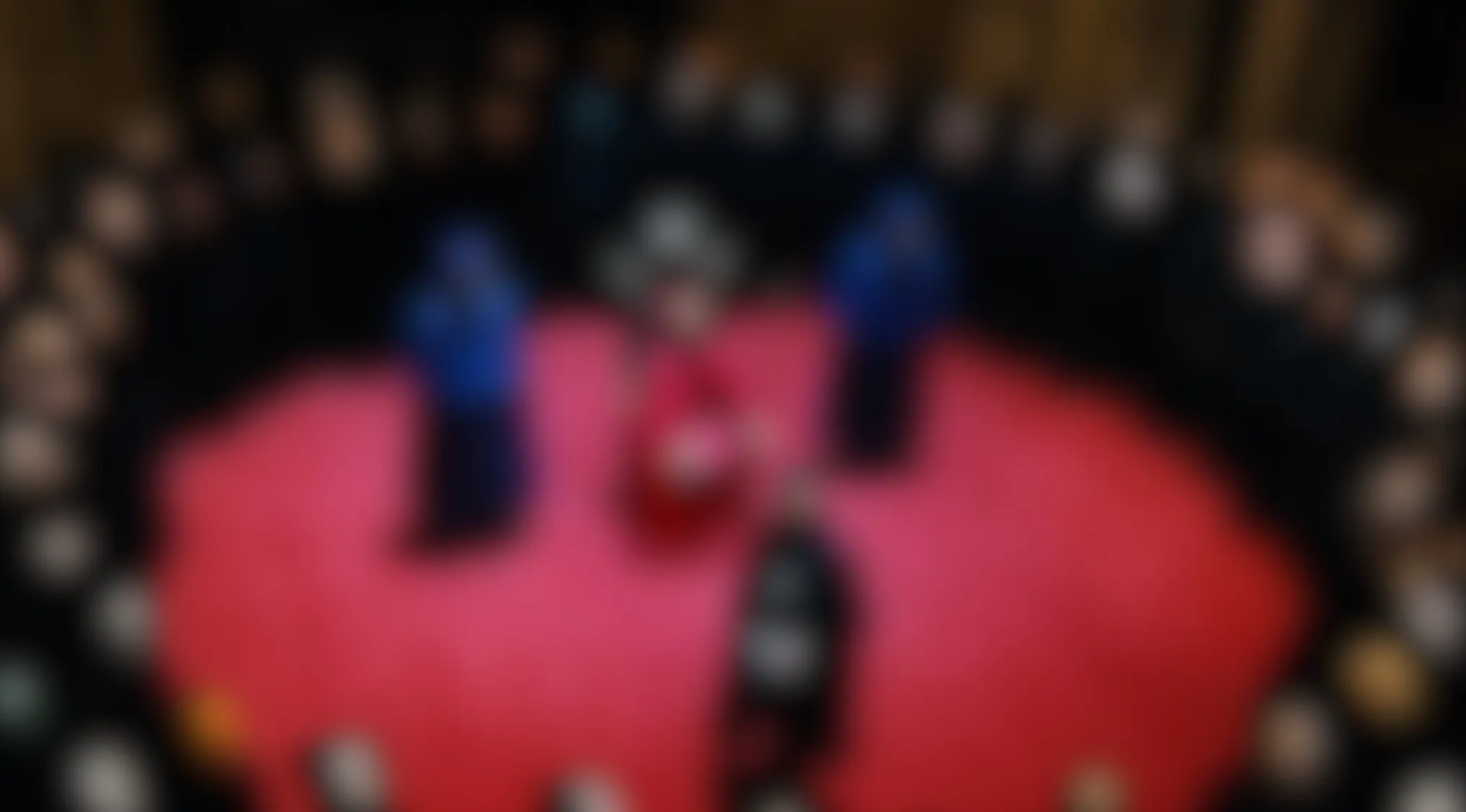 Blurry Movie Scenes: A red circular stage with several indistinct figures in red, blue, and black, surrounded by an audience.