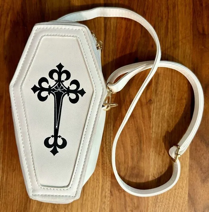 A white coffin-shaped purse with a black cross design, found in the Goodwill bins.
