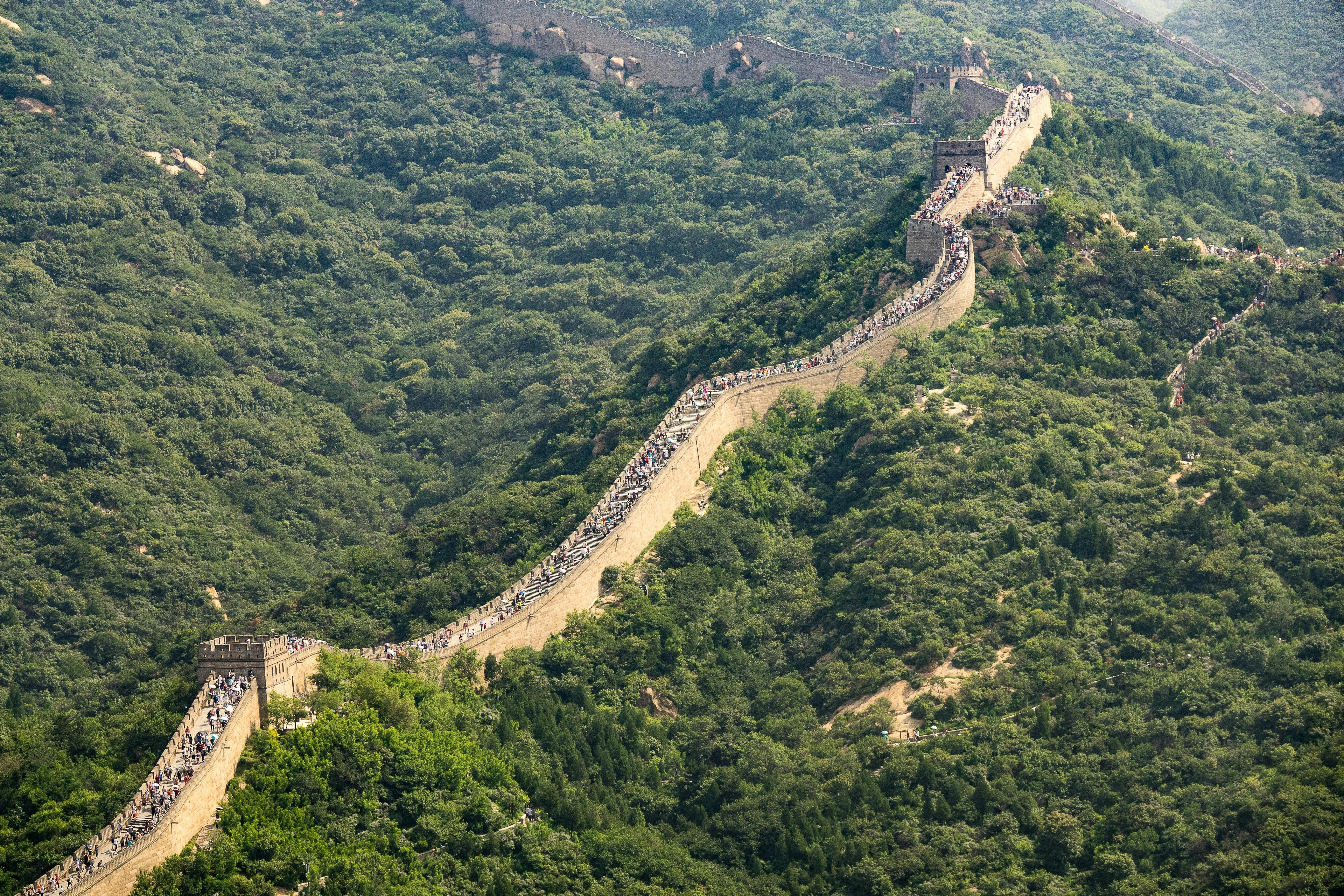 Crowded Great Wall of China snaking through lush mountains. A famous landmark for a Geography Challenge: Guess the country.