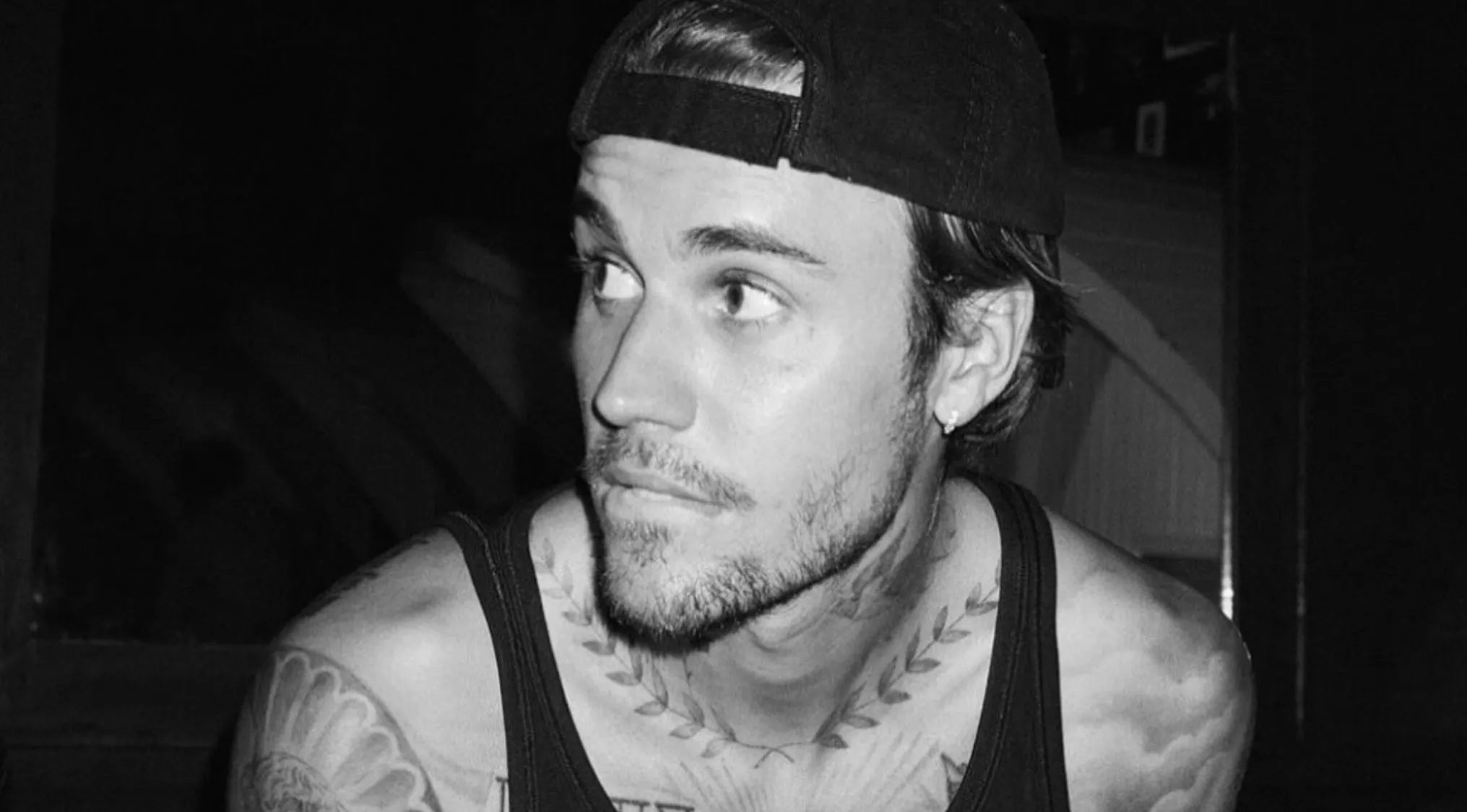 Black and white photo of a famous person, Justin Bieber, with tattoos & beard, wearing a cap. Guess The Country.